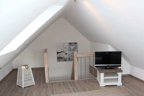 A room with a sloped ceiling, a television on a wooden stand, and a small table. - Holiday home with 2 bedrooms (Greetsiel)