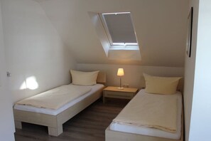 A small, single-room accommodation with two beds, a skylight, and a bedside table with a lamp. - Holiday home with 2 bedrooms (Greetsiel)
