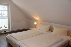 A bedroom with a sloped ceiling, a bed with white bedding, a bedside lamp, and a window with a view of the outside. - Holiday home with 2 bedrooms (Greetsiel)