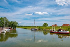 A calm river with boats docked, a grassy bank, and a clear sky. - Holiday apartment with 2 bedrooms (Hooksiel)