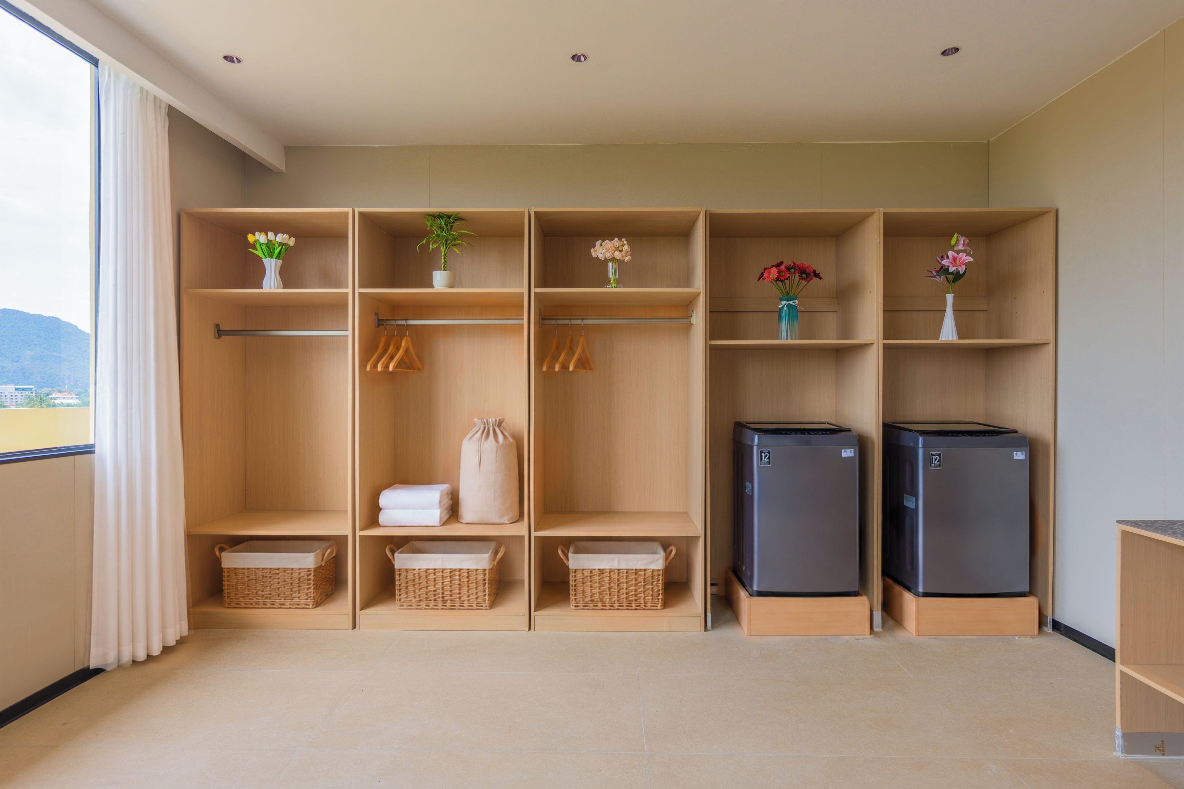 Una habitación moderna y bien organizada con un ventanal grande, un armario con varios compartimentos, dos refrigeradores y cestas de mimbre.