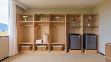Una habitación moderna y bien organizada con un ventanal grande, un armario con varios compartimentos, dos refrigeradores y cestas de mimbre.