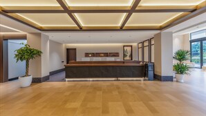 A reception area with a wooden reception desk, potted plants, and a large window providing a view of the outdoors. - Vangvieng THAVIKUN HOTEL (Vang Vieng)