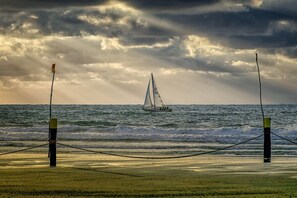 Ein Strand mit einer Seilsperre und einem Segelboot in der Ferne.