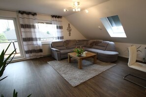 A modern living room with a sectional sofa, a coffee table, and a window with curtains. - Holiday apartment with 1 bedroom (Rhauderfehn)