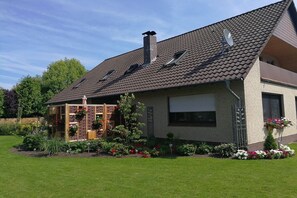 A two-story house with a sloped roof, a brick exterior, and a garden with various plants and flowers. - Holiday apartment with 1 bedroom (Rhauderfehn)