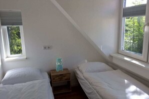 Ein Schlafzimmer mit zwei Einzelbetten, einem Nachttisch aus Holz und einem Fenster mit Blick auf Bäume.