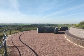 Uma passarela pavimentada com um corrimão curvo, conduzindo a uma plataforma de observação com vista ampla da paisagem.