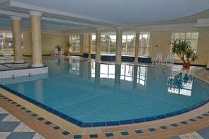 An indoor swimming pool with clear water, surrounded by columns and potted plants. - 120 Kurpark Residenz Cuxhaven (Cuxhaven)