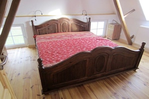 A bedroom with a wooden bed, a red patterned bedspread, and a sloped ceiling. - Holiday home with 4 bedrooms (Burhave\/Butjadingen)
