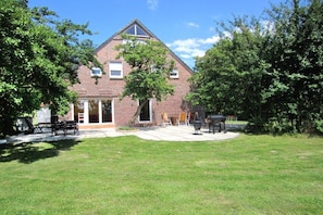 A brick building with a triangular roof, a covered patio area with outdoor furniture, and a well-maintained lawn. - Holiday home with 4 bedrooms (Burhave\/Butjadingen)