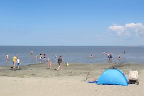 A beach with a tent and a cart, people swimming and walking on the sand. - Holiday home with 4 bedrooms (Burhave\/Butjadingen)