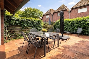 An outdoor patio with a table and chairs, surrounded by a brick wall and greenery. - Holiday apartment with 3 bedrooms (Dangast)