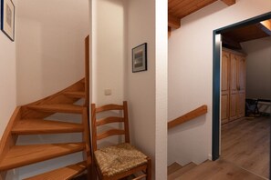 Eine Holztreppe mit einem Sessel, einem gerahmten Bild an der Wand und Blick in einen Raum mit Holzschränken.