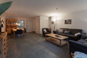 A living room with a sofa, a coffee table, and a dining area with chairs and a cabinet. - Holiday apartment with 3 bedrooms (Dangast)