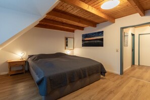Un dormitorio con techo inclinado, una cama, una mesita de noche, un cuadro en la pared y una puerta.