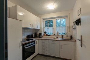 A modern kitchen with white cabinetry, a built-in oven, a sink, and a window with a view of trees. - Holiday apartment with 3 bedrooms (Dangast)