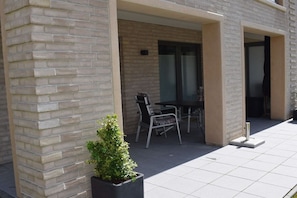 An outdoor seating area with a table and chairs, a potted plant, and a building entrance. - Holiday apartment with 1 bedroom (Dangast)