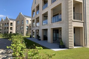 A modern multi-story residential building with balconies, a well-maintained lawn, and a clear sky. - Holiday apartment with 1 bedroom (Dangast)