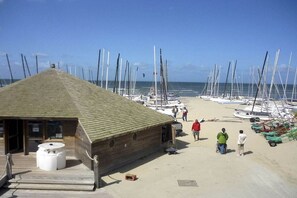 A wooden building with a sloped roof, a small outdoor seating area, and a beachside view with multiple sailboats docked. - Holiday apartment in Koksijde with Wi-Fi (Koksijde)