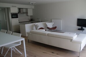 A modern kitchen with white cabinetry, a dining area with a white table and chairs, and a living area with a white sofa and two red chairs. - Holiday apartment in Koksijde with Wi-Fi (Koksijde)