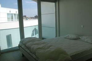 A bedroom with a large window, a bed, and a view of the city. - Holiday apartment in Koksijde with Wi-Fi (Koksijde)