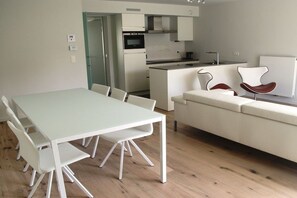 Cozinha moderna com armários brancos, forno embutido e área de refeições com mesa e cadeiras brancas.