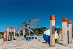 A beach with a large umbrella structure, wooden posts with numbers, and a beach ball. - Small Horizon 101 Renesse (Renesse)