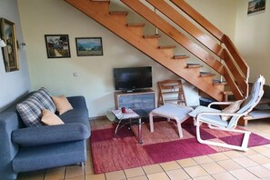 A living room with a sofa, a television, a wooden staircase, and a lounge chair. - Holiday home with 2 bedrooms (Clausthal-Zellerfeld, Buntenbock)