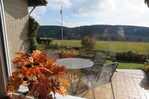 A patio with a round table and chairs, a view of a green field, and a brick wall. - Holiday home with 2 bedrooms (Clausthal-Zellerfeld, Buntenbock)