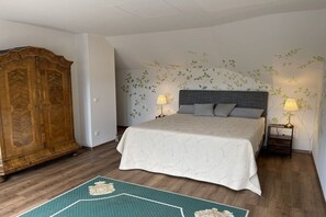 A bedroom with a large bed, two bedside lamps, a wooden wardrobe, and a wall with leaf patterns. - Holiday apartment with 1 bedroom (Mondsee)