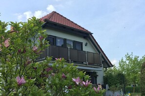 A two-story house with a red-tiled roof, a balcony on the upper floor, and a garden with flowering plants in front. - in an idyllic location in Klink (Klink)