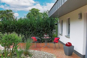 A patio with a table and chairs, surrounded by greenery and a white building. - Holiday home in Waren with swimming pool (Waren)