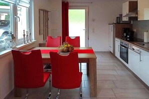 Eine moderne Küche mit weißen Schränken, einer Holzausziehtafel und einem roten Esstisch mit passenden Stühlen.