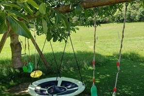 A swing set with a circular seat suspended by ropes, a tree trunk, and a grassy field in the background. - Alpine Glow Schranzlhof (Hollersbach)