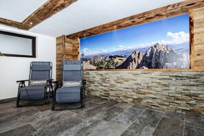 A room with a stone wall and a large mountain landscape painting. There are two chairs with a logo on them. - Alpine Glow Schranzlhof (Hollersbach)