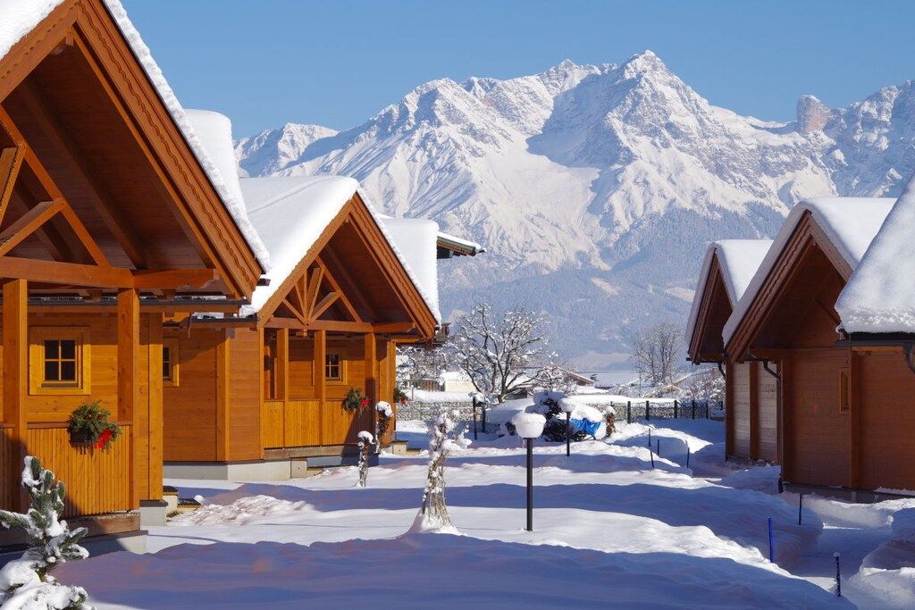 Eine Holzhütte mit verschneitem Dach, vor einer Kulisse schneebedeckter Berge.