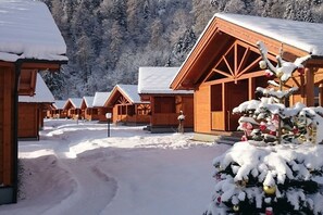 Eine Reihe von Holzhütten mit schneebedeckten Dächern, vor einer Kulisse aus mit Schnee beladenen Bäumen.