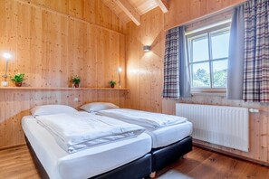 A wooden-paneled room with two beds, a window with curtains, and a radiator. - Cabin in Maishofen with swimming pool (Maishofen)