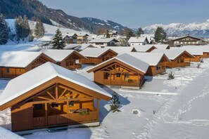 A row of wooden cabins with snow-covered roofs, set against a backdrop of snow-covered mountains. - Cabin in Maishofen with swimming pool (Maishofen)