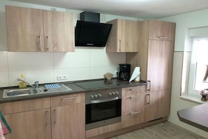 Een keuken met houten kastjes, een inbouwoven, een koffiezetapparaat en een raam.