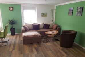 Een woonkamer met een bank, een salontafel, een stoel, een potplant en kunst aan de muren.