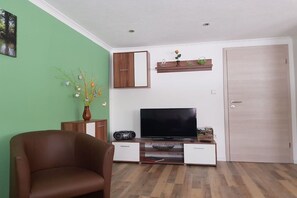 Ein Wohnzimmer mit braunem Sofa, einem Flachbildfernseher, einem Holzschrank und einer Tür.