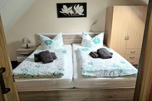 Een tweeepersoonskamer met twee bedden, elk voorzien van beddengoed en handdoeken met bloemendesign, een bedlampje en een houten garderobe.