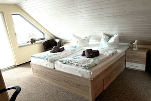 Ein Schlafzimmer mit einem hölzernen Bett, einem Fenster, einem Sessel und einem Nachttisch.