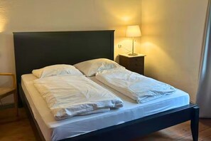 Ein Einzelbett mit dunklem Kopfteil, ein Nachttisch mit Lampe und ein Holzstuhl.