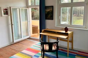 A room with a wooden desk, a chair, a colorful striped rug, and a window with a view of greenery.