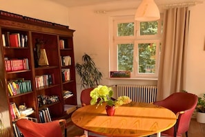A room with a wooden bookshelf, a round table with a vase of flowers, and a window with curtains.