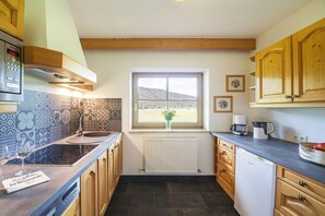 Eine Küche mit Fenster, einem eingebauten Herd, Holzschränken und einer gefliesten Spritzschutzwand.