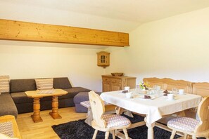 Een gezellige woonkamer met een houten plafond, een bank, een eettafel met stoelen en een klein kastje.